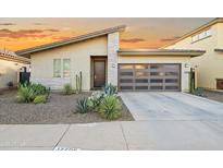 Stylish single-story home featuring desert landscaping, a modern garage door, and a neutral color palette against a vibrant sunset sky at 17706 N Rosa Dr, Maricopa, AZ 85138