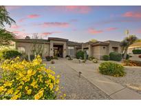 Inviting single-story home with desert landscaping, paver walkway, and a cozy covered porch, accentuated by a colorful sunset at 9534 E Monument Dr, Scottsdale, AZ 85262