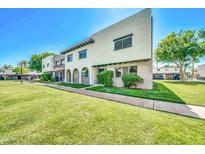 Charming townhome featuring stucco walls, red tile accents, a lush green lawn, and mature trees against a clear blue sky at 2812 E Clarendon Ave, Phoenix, AZ 85016