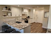 Open kitchen features granite counters, a gas range, breakfast bar, subway tile backsplash, and white cabinetry at 10284 E Mallow Cir, Scottsdale, AZ 85255