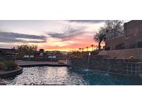 Inviting pool area with a stone waterfall feature and built-in seating, set against a vibrant sunset backdrop at 136 E Desert Wind Dr, Phoenix, AZ 85048