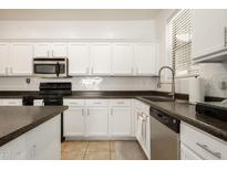 Bright kitchen features white cabinets, black appliances, and dark countertops at 17613 N 114Th Ln, Surprise, AZ 85378