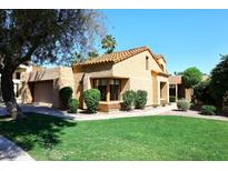 Tan single-story home with tile roof, manicured lawn, mature trees, and a two car garage at 9115 N 101St Way, Scottsdale, AZ 85258