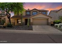Charming two-story home boasts a desert landscape, mature tree, and tile roof under a vibrant sunset sky at 10329 E Star Of The Desert Dr, Scottsdale, AZ 85255