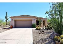 Tan single-story home featuring a two-car garage, desert landscaping, and a tile roof at 6966 E Bramble Berry Ln, Scottsdale, AZ 85266