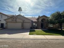 Charming single-story home with a three-car garage, lush lawn, and a beautifully landscaped yard with a palm tree at 2301 E Beachcomber Dr, Gilbert, AZ 85234