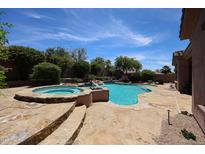 Beautiful pool with a rock waterfall feature and integrated hot tub, surrounded by desert landscaping at 17975 W Willow Dr, Goodyear, AZ 85338
