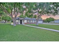 Charming single-story home featuring a lush green lawn, mature shade trees, and a welcoming front porch with rocking chairs at 1886 S 141St Pl, Gilbert, AZ 85295