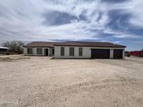 An exterior of a one-story white home with a brown roof and three-car garage situated on a large gravel lot at 29935 W Roosevelt St, Buckeye, AZ 85396