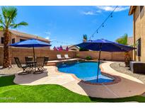 Beautiful backyard pool featuring a rock waterfall, lounge chairs, outdoor seating, and a lush green lawn at 16565 W Garfield St, Goodyear, AZ 85338