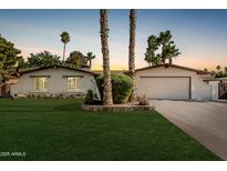 Charming single-story home featuring a lush front lawn, mature palm trees, and a two-car garage at 5333 E Sheena Dr, Scottsdale, AZ 85254