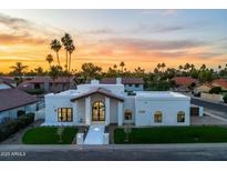 The home has a bright exterior with a grand entrance and manicured lawn, complemented by palm trees and a colorful sunset backdrop at 9820 N 87Th Pl, Scottsdale, AZ 85258