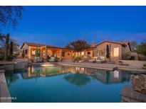 A stunning backyard oasis featuring a pool, outdoor seating, and beautifully lit landscaping at twilight at 5712 E Blue Sky Dr, Scottsdale, AZ 85266