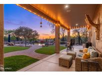 A covered patio with comfortable seating overlooks the backyard, pool, and desert landscaping at sunset at 5712 E Blue Sky Dr, Scottsdale, AZ 85266