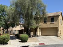 Tan two-story home featuring a two-car garage, driveway, and mature shade trees at 9456 W Jamestown Rd, Phoenix, AZ 85037