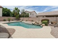 Beautiful kidney-shaped pool features rock waterfall, concrete surround and desert landscaping at 2834 E Devon Ct, Gilbert, AZ 85296