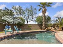 Backyard pool with a stone waterfall, lush landscaping, and two chairs under an umbrella at 21362 E Puesta Del Sol Rd, Queen Creek, AZ 85142