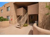 Exterior view of a tan building with concrete walkway and staircase leading to upper level condos in a lush landscape at 8155 E Roosevelt St # 205, Scottsdale, AZ 85257