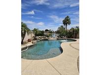 Beautiful backyard pool with rock waterfall feature and lush tropical landscaping overlooking a lake at 7724 W Topeka W Dr, Glendale, AZ 85308