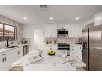 Bright kitchen features white cabinetry, stainless steel appliances, and a marble countertop island at 10625 E Bramble Ave, Mesa, AZ 85208