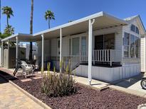 Charming mobile home with covered porch, manicured landscape, and palm trees against a vibrant blue sky at 1226 S Seneca Dr, Apache Junction, AZ 85119