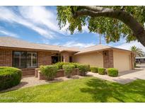 Charming single-story brick home featuring a well-manicured lawn, mature trees, and an attached two-car garage at 13055 W Tangelo Dr, Sun City West, AZ 85375