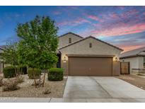 Single-story home featuring a well-manicured front yard, neutral tones, and a two-car garage, set against a beautiful sunset sky at 17573 W Via De Luna Dr, Surprise, AZ 85387