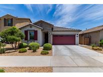 Charming single-story home boasts a red garage door, complemented by fresh landscaping and blue skies at 25289 N 143Rd Dr, Surprise, AZ 85387