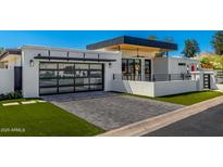 Modern home exterior featuring a glass garage door, gray brick driveway, and manicured lawn at 5822 N 44Th Pl, Phoenix, AZ 85018