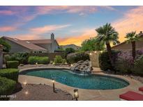 A stunning pool with a rock waterfall feature surrounded by lush landscaping and a captivating sunset sky at 4428 E Yawepe St, Phoenix, AZ 85044