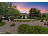 Stunning home exterior with lush landscaping, gravel driveway, and a picturesque desert sunset backdrop at 7002 E Aster Dr, Scottsdale, AZ 85254