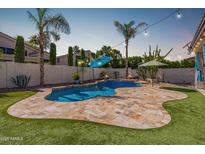 Sparkling pool with baja shelf, lush turf, travertine tile, and string lights create an entertainer's backyard at 3190 S Holguin Way, Chandler, AZ 85248