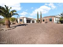 Stunning home featuring a stone and stucco exterior, a spacious brick driveway, and mature desert landscaping with palm trees at 13648 E Aloe Vera Dr, Scottsdale, AZ 85262