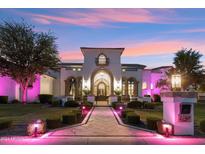 Elegant stucco home with manicured lawn, illuminated walkway, and decorative wrought iron gate in the evening at 2748 E Warbler Rd, Gilbert, AZ 85297