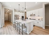 Bright, white kitchen with modern appliances, a large island with seating, and wood-look floors at 1865 N 141St Ave, Goodyear, AZ 85395