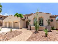 Elegant stucco home showcasing a three-car garage, desert landscaping, and a charming arched entryway at 915 W Orchard Ln, Litchfield Park, AZ 85340