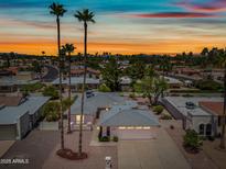 Charming single-story home boasts a well-manicured lawn, a driveway, and picturesque palm trees at sunset at 9654 E Foster Ave, Sun Lakes, AZ 85248