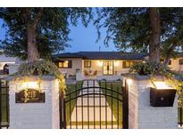 Charming home exterior with a black iron gate, manicured lawn, and illuminated entryway at dusk at 4215 E Flower St, Phoenix, AZ 85018
