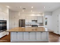 Bright white kitchen featuring stainless steel appliances, a large island with granite countertops, and hardwood floors at 5832 E Bent Tree Dr, Scottsdale, AZ 85266