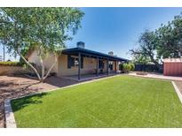 Large backyard featuring manicured turf, covered patio, firepit, and mature trees at 3251 W Mercer Ln, Phoenix, AZ 85029
