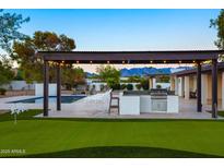 Outdoor kitchen with stainless steel grill, and a pergola with lights near a pool and putting green at 13620 N 80Th Pl, Scottsdale, AZ 85260