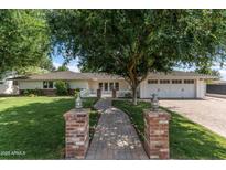 Charming home featuring a brick walkway, lush lawn, white picket fence, and large tree, with a two-car garage at 3817 E Highland Ave, Phoenix, AZ 85018