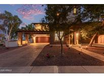 Two-story home with a brick driveway, stone accents, and balcony situated over the garage, beautifully lit at dusk at 20689 W Valley View Dr, Buckeye, AZ 85396