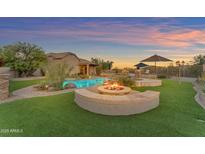 Stunning backyard with a pool, fire pit, and lush landscaping perfect for outdoor entertaining in the evening at 18199 W Buckhorn Dr, Goodyear, AZ 85338