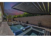 An inviting pool featuring a modern pergola and tranquil fireplace under a vivid twilight sky at 199 E Tangerine Path, Queen Creek, AZ 85140