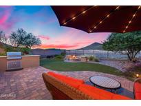 Outdoor living space with built in grill, fire pit and patio furniture under a lighted umbrella at sunset at 32359 N 129Th Dr, Peoria, AZ 85383
