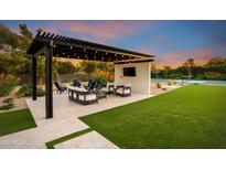 Beautiful backyard patio features a covered lounge area, green lawn, and a luxurious tennis court for outdoor recreation at 8001 E Voltaire Ave, Scottsdale, AZ 85260