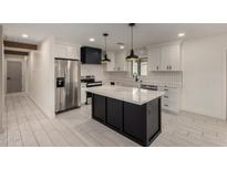Modern kitchen boasts white cabinets, a black island with marble countertop, and stainless steel appliances at 313 N 101St Way, Mesa, AZ 85207
