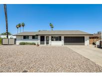 Charming single-story home features a gravel yard, black garage door, and palm trees in a sunny setting at 9214 N 54Th Ave, Glendale, AZ 85302
