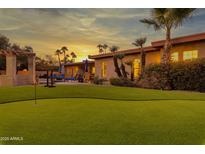 Beautiful backyard featuring a putting green, pool, palm trees, patio, and a colorful sunset at 6043 E Hearn Rd, Scottsdale, AZ 85254
